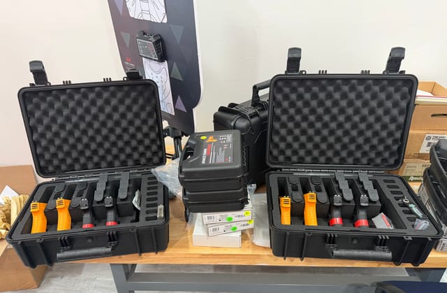 Two open Pelican cases on a table, each holding four laser-equipped training pistols, with simulator projector in the background